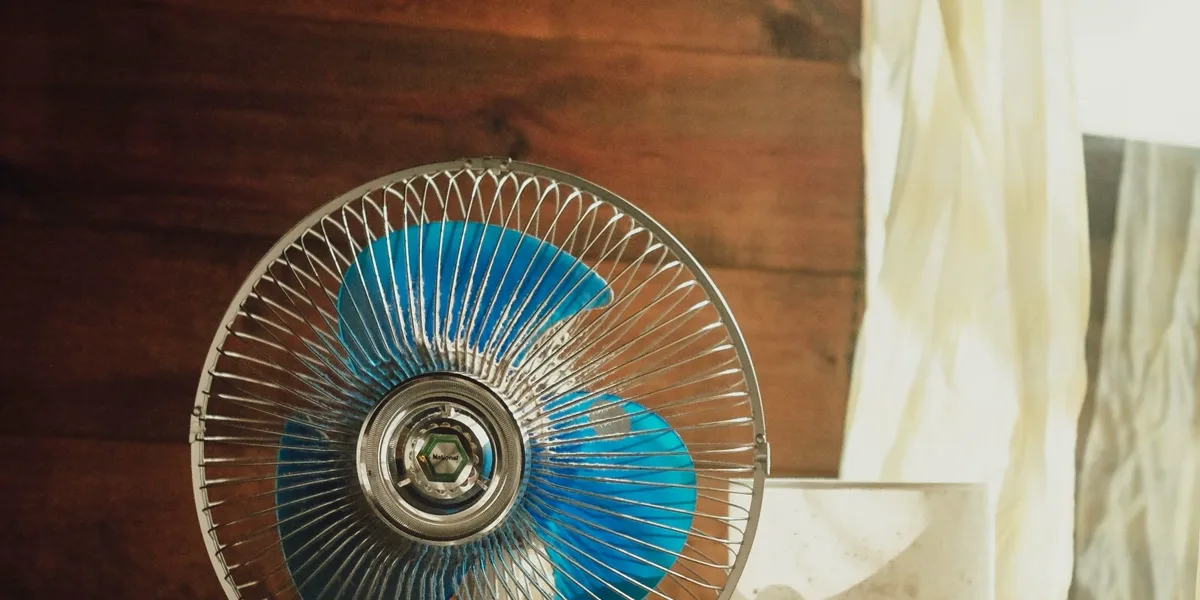 A classic desk fan beside a sunlit window with a sheer curtain